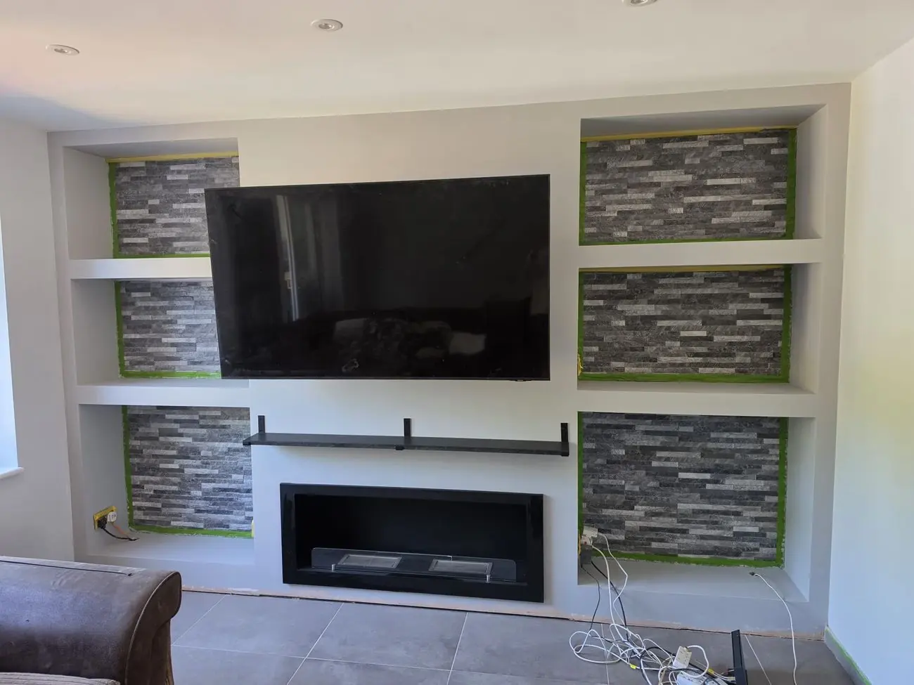 The finished media wall with stone-clad recesses, concealed lighting and a fire